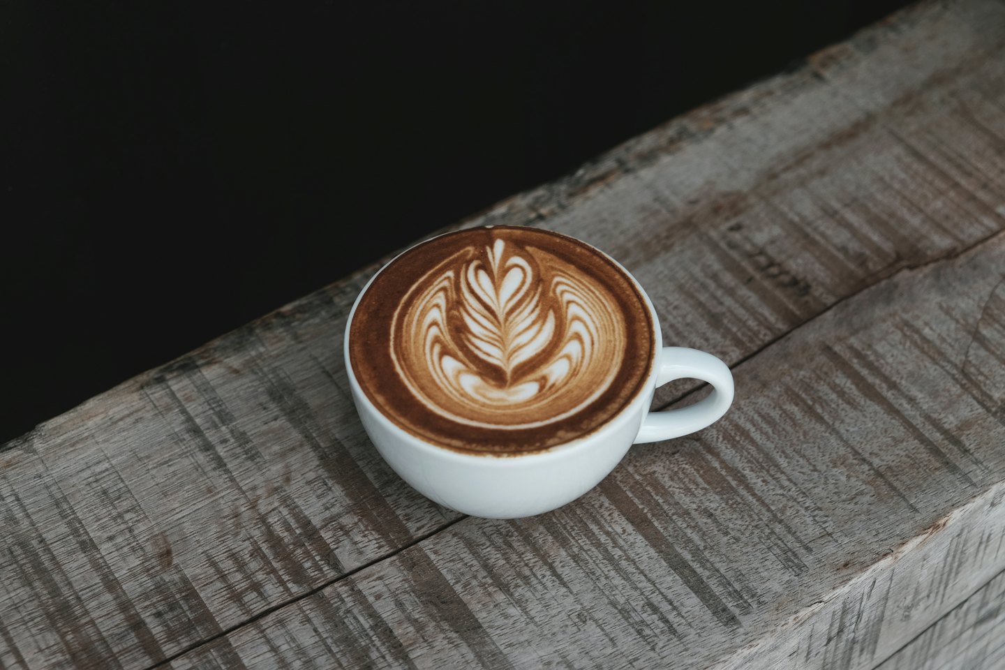 White coffee mug with latte art on a wooden table.
