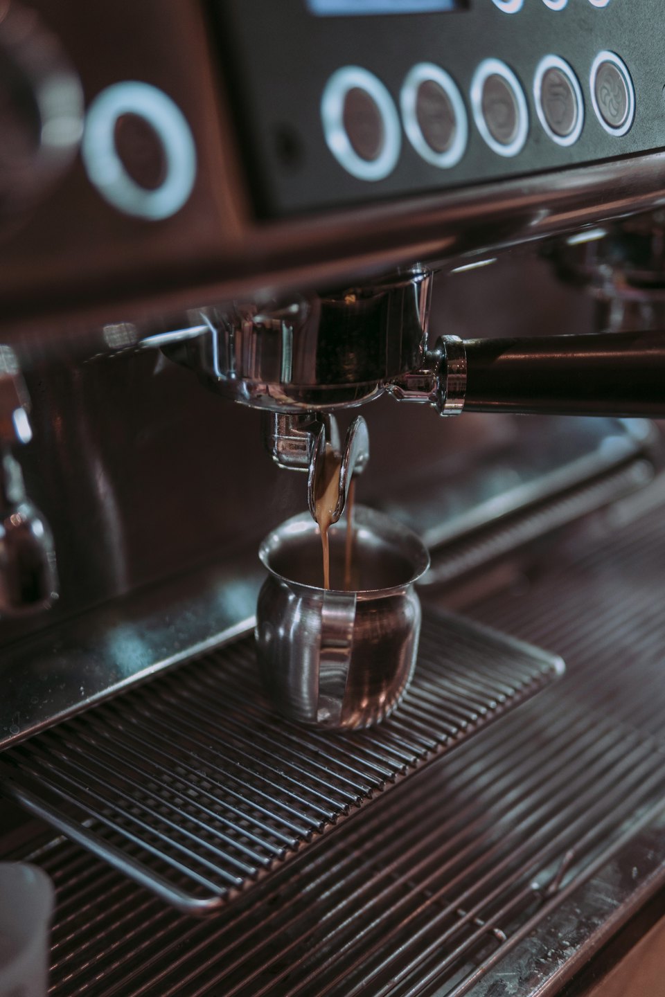 Espresso coffee pours from a portafilter into a metal cup.