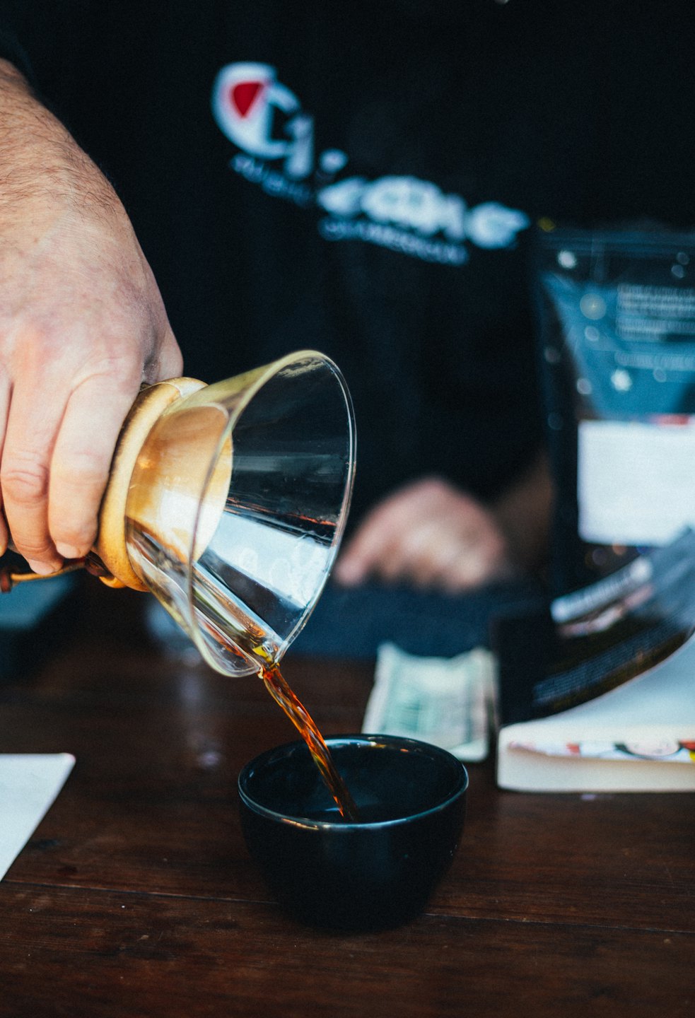 Hand pouring coffee from glass pour-over into ceramic cup.