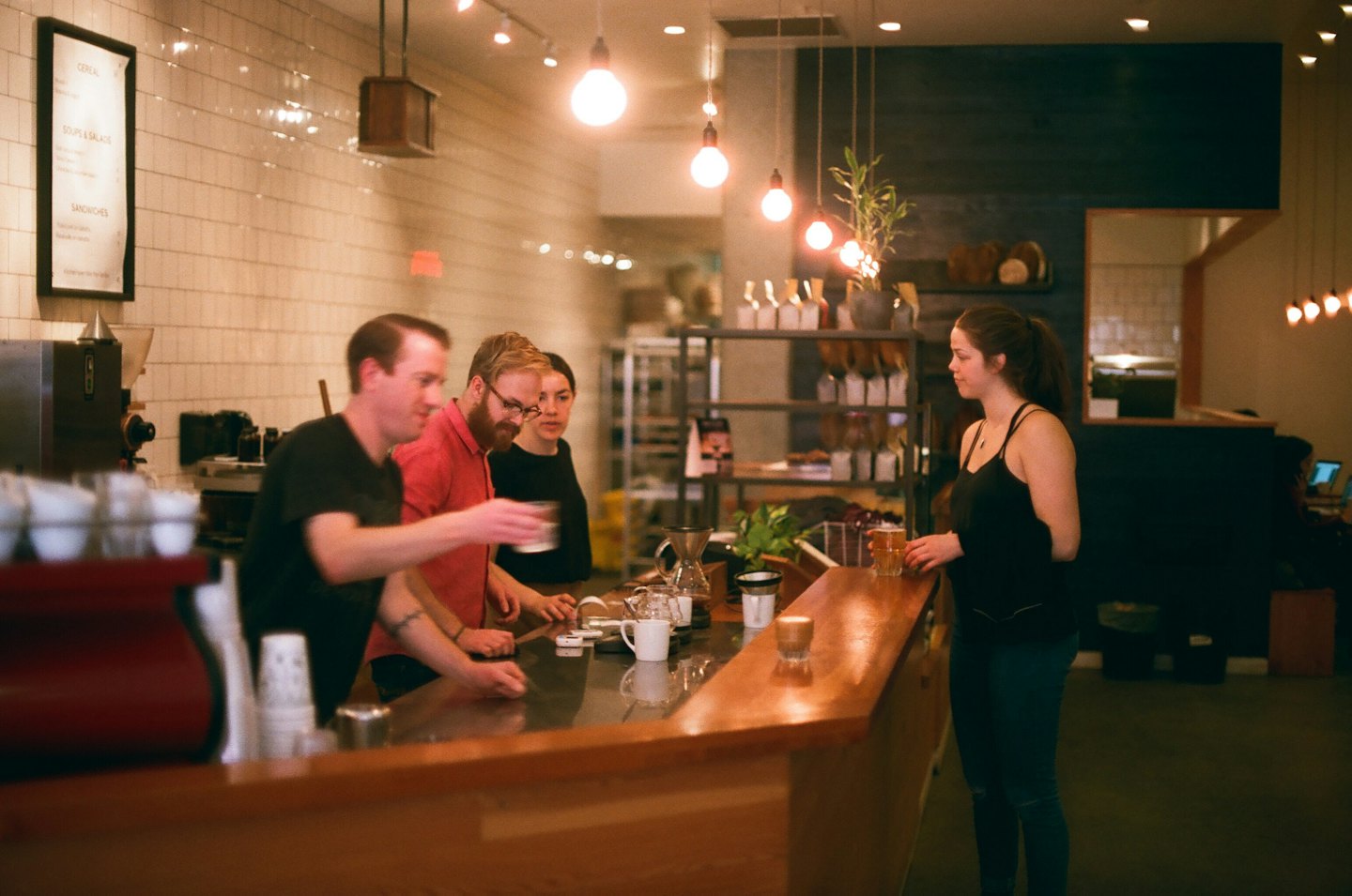 Barista serves customers at a warmly lit cafe counter.