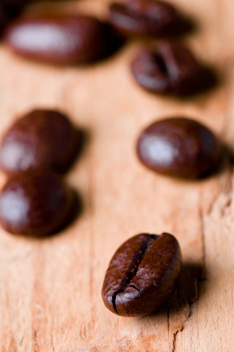 Dark roasted coffee beans scattered across a wooden surface.