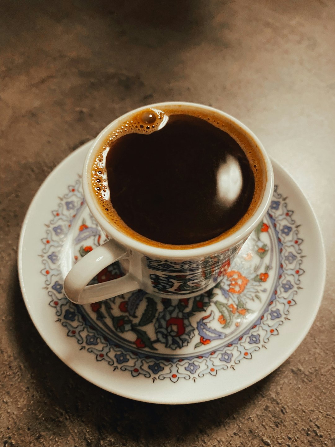 Patterned coffee cup and saucer sitting on a dark table.
