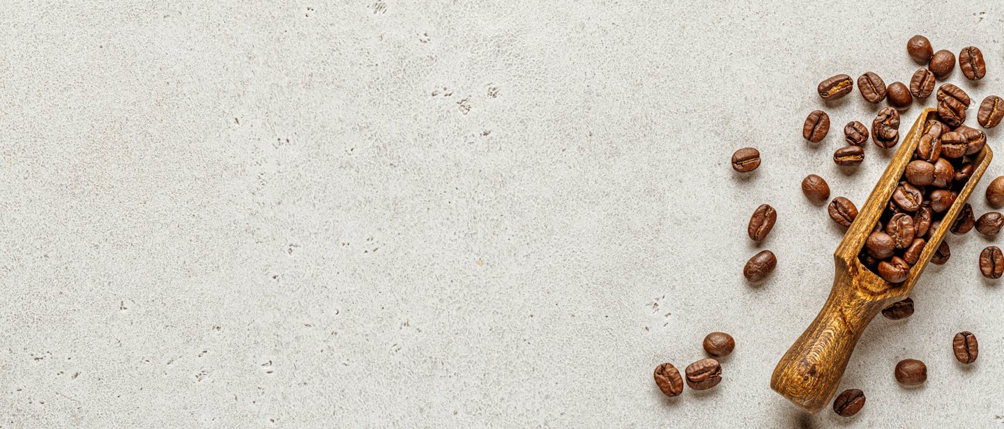 Roasted coffee beans in a small wooden scoop on a stone surface.
